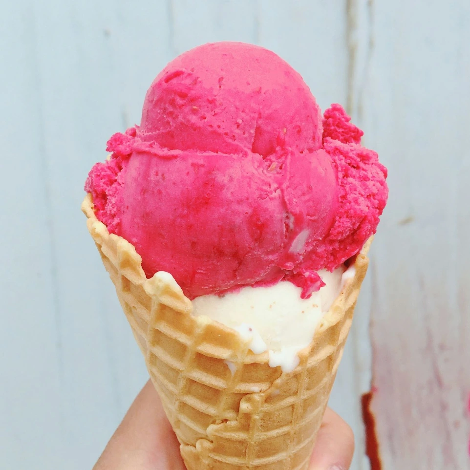 person holding ice cream cone with pink ice cream